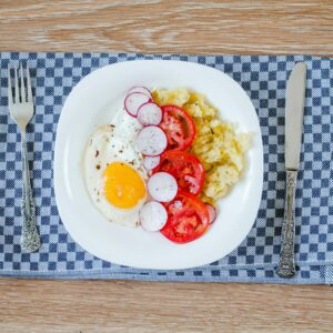 A delicious breakfast featuring fried eggs, tomatoes, radishes, and smashed potatoes.