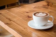 Close-up of a white cup of latte with artistic foam on a rustic wooden table.