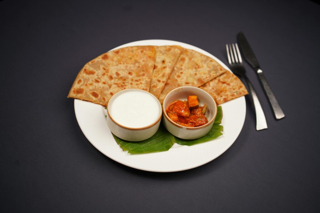 Tasty Indian paratha served with pickle and yogurt on a white plate with cutlery.
